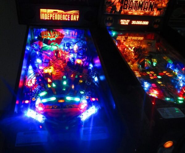 Colorful pinball machines lit in dark arcade