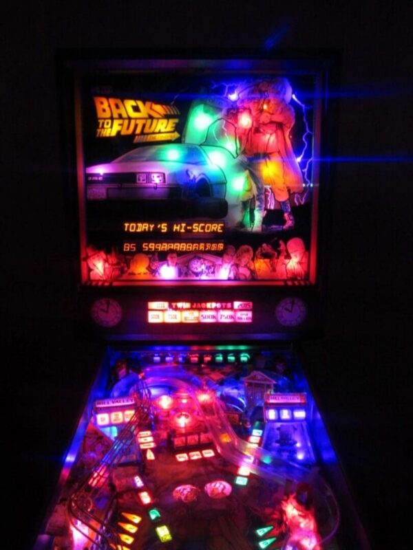 A lighted pinball machine in the dark with lights on.