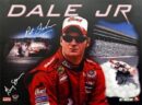 A man in red racing suit sitting on the side of a race track.